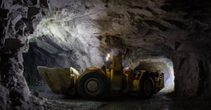 A yellow mining machine navigates hard rock tunnels. It's dark in the tunnels, but the machine's light illuminates the way.