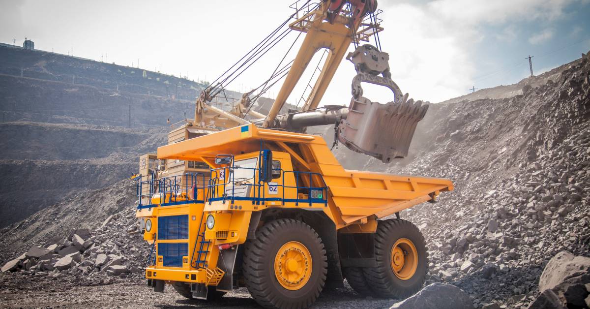 A mining vehicle moves around different materials at the mine site. There are lots of rocks and clouds in the background.