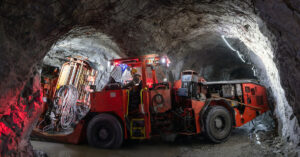 A large orange underground mining vehicle navigates deep and dark mining tunnels with a large light.