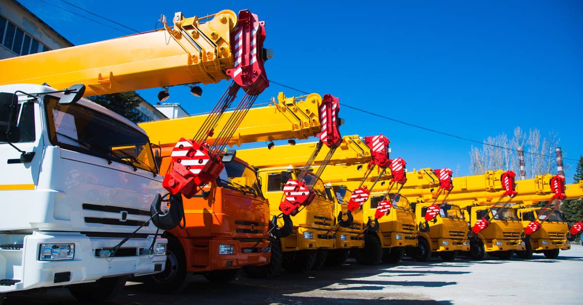 Mobile cranes are parked beside one another. Each one has a telescopic arm hooked to the front of the crane.