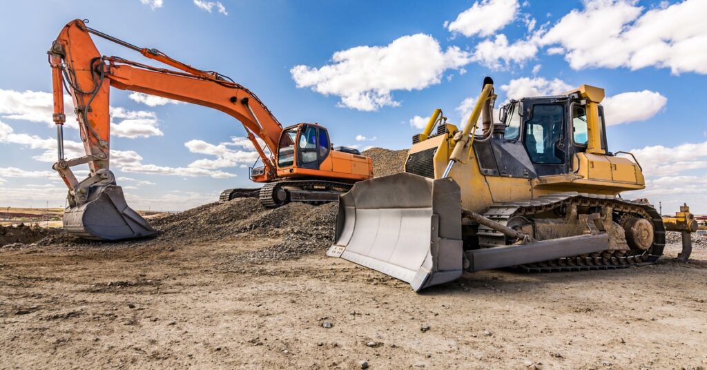 Two large yellow unattended mining vehicles are parked in a flattened dirt lot under a partly cloudy sky.