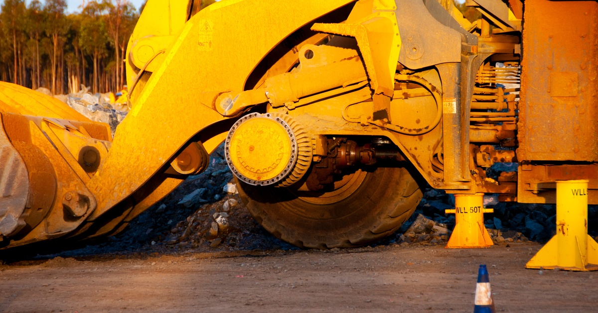A close-up of a yellow mining vehicle with large tires and a bucket attached to its front working outdoors.