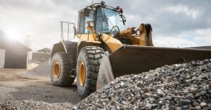 A mining front loader parked outdoors in a gravel lot. The bucket is near a large pile of gravel and rocks.