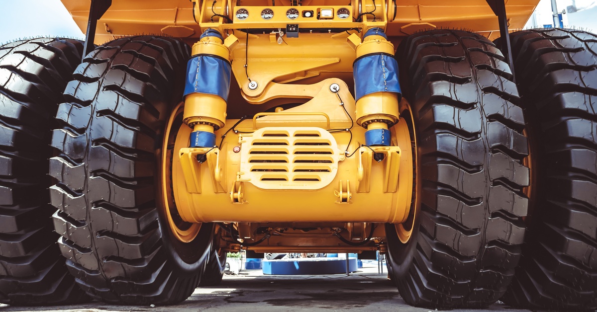 The underside of a yellow industrial vehicle with four large black tires on one end parked outside on pavement.
