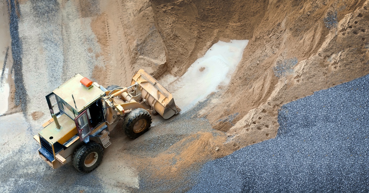 An overhead view of a yellow bulldozer with four large wheels digging through piles of sand and gravel.