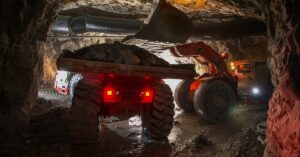 Two off-highway vehicles operating together inside a mine with their lights illuminating nearby tunnels.