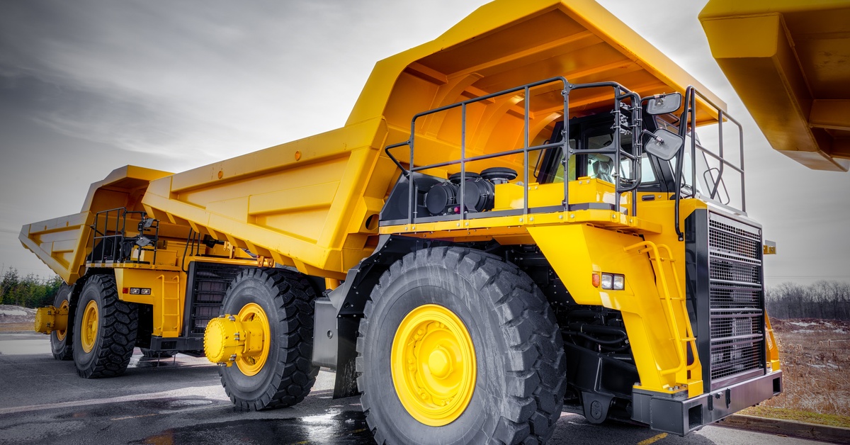 Three identical yellow mining vehicles with large tires and a black railing are parked in a row outdoors.