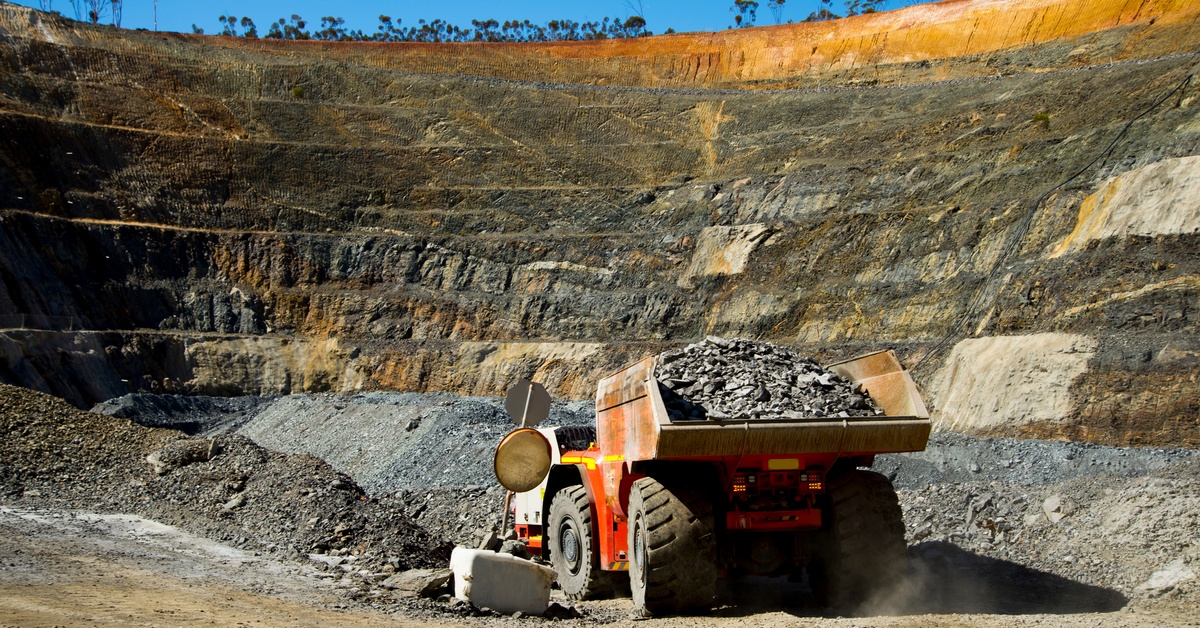 A large mining vehicle hauling a bed full of gravel and rocks is parked in the middle of a dirt trench.