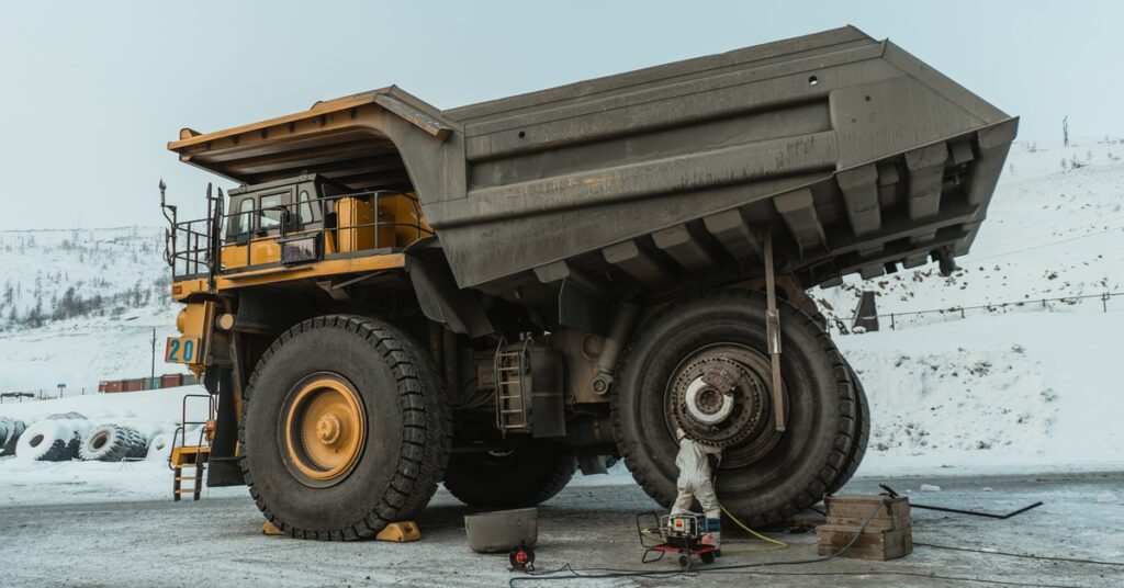 An industrial mining dump truck parked on snowy terrain. There is a technician near a back wheel of the truck.