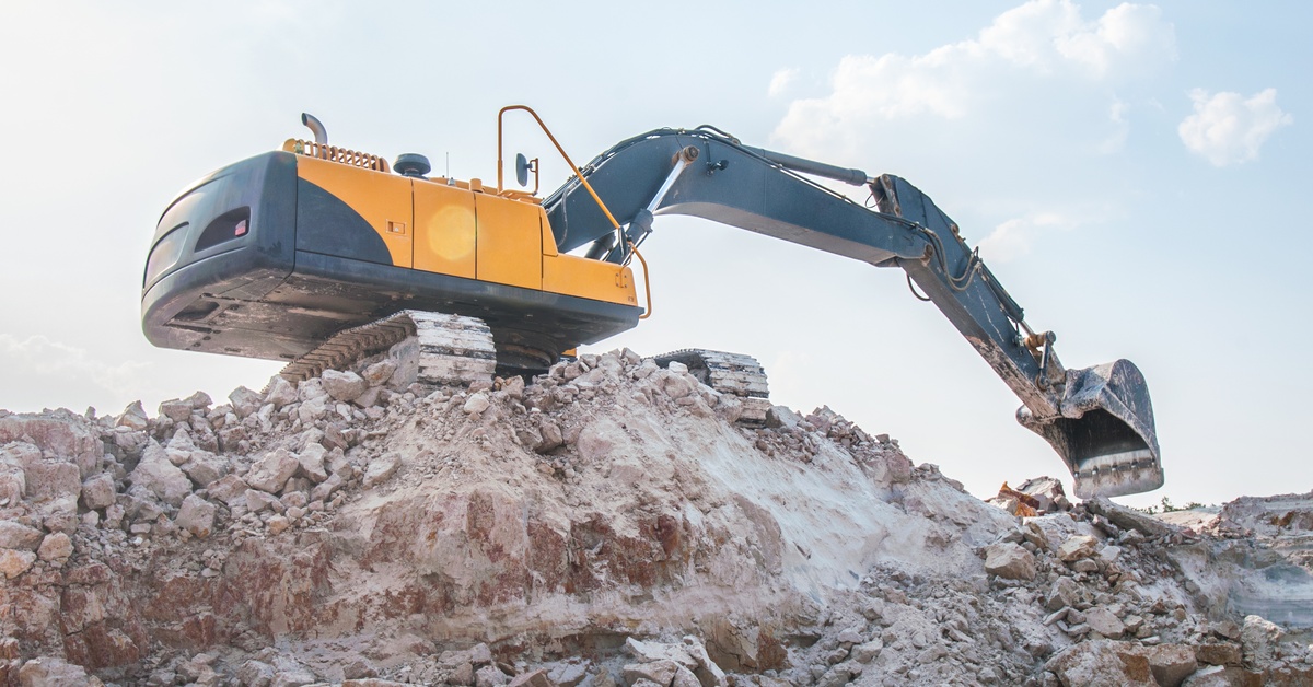 A large yellow loader excavator sitting on the top of a sandpit. It's dusty and there are some clouds in the background.
