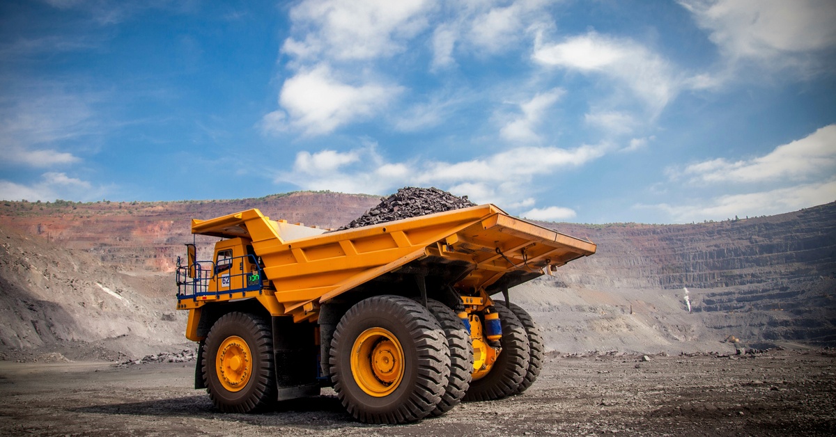 A yellow mining vehicle alone in the middle of a mining pit, hauling ore in the back of the vehicle.