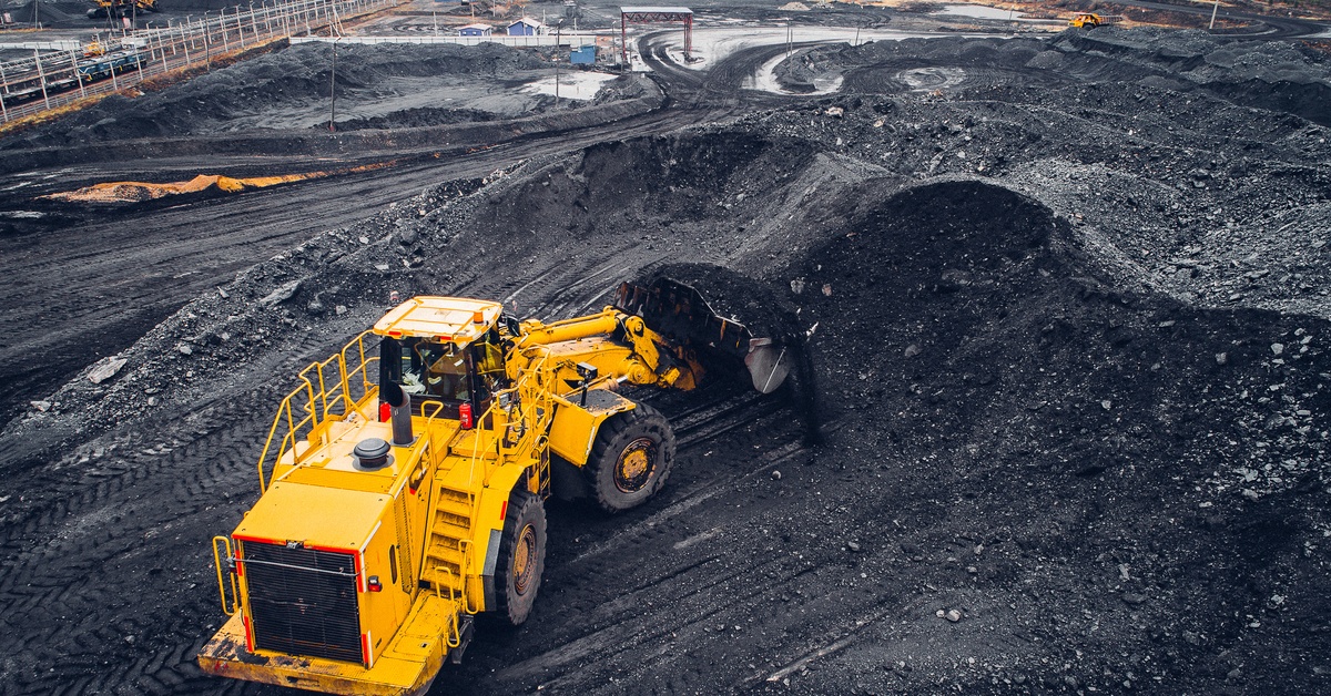 A yellow mining vehicle pushing a large pile of coal dust upward. The machine creates a hill of coal.