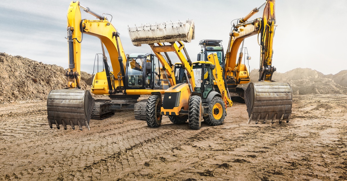 Excavators, dump trucks, and bulldozers are parked beside one another in a muddy area covered with tire tread marks.