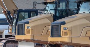 Multiple yellow heavy-duty construction vehicles are sitting next to each other with trees in the background.
