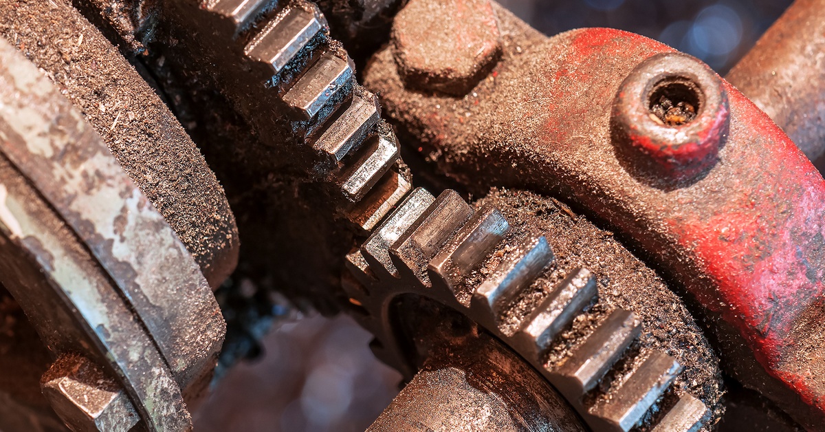 A close-up view of two gears connected to each other. Each gear is covered in dark orange and brown rust.