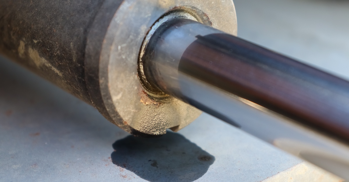 A close-up view of a hydraulic piece of equipment with oil leaking out, staining the surface it's on top of.