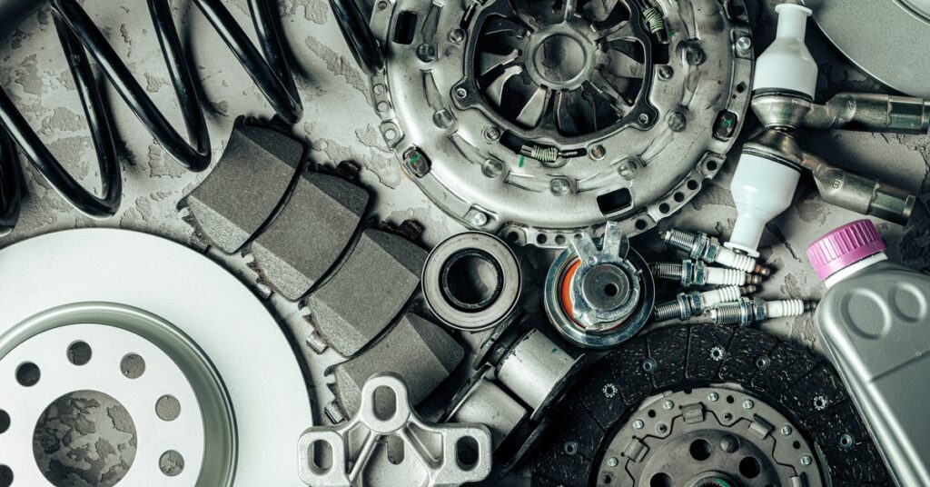 A close-up of spare car parts lying next to each other, including springs, gears, and a bottle of fluid with a purple cap.