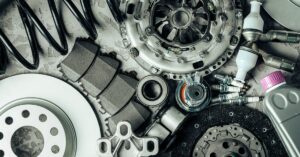 A close-up of spare car parts lying next to each other, including springs, gears, and a bottle of fluid with a purple cap.