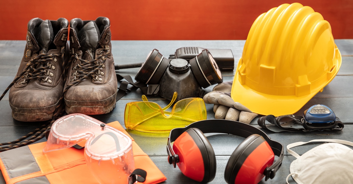 Personal protective equipment sits on a table, including a hard hat, goggles, boots, a respirator, and a mask.