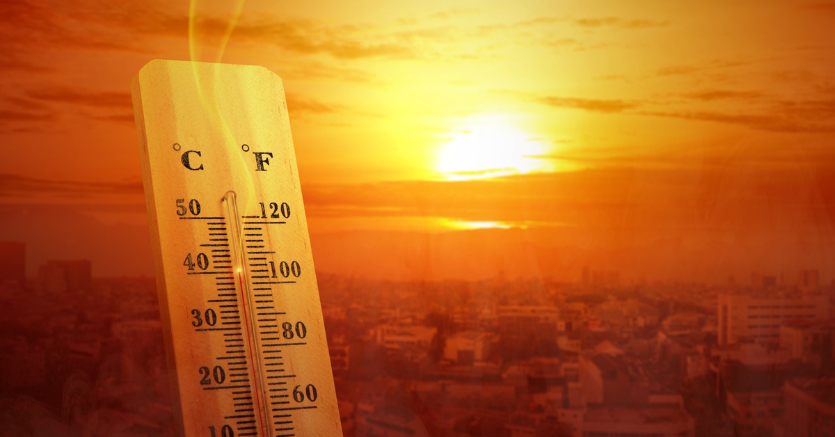 The sun sets and casts an orange glow over a city with a thermometer in the foreground showing high temperatures.