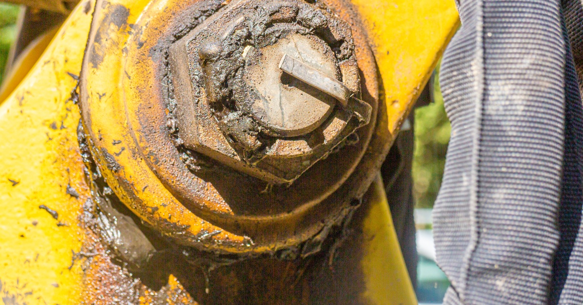 A close-up of the joint on a large yellow piece of industrial equipment with brown grease coming out.