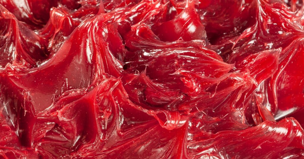 A highly detailed, close-up view of red industrial grease. The grease has sharp peaks and a glossy sheen.
