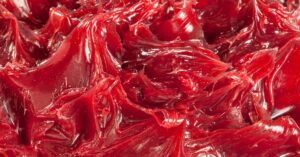 A highly detailed, close-up view of red industrial grease. The grease has sharp peaks and a glossy sheen.