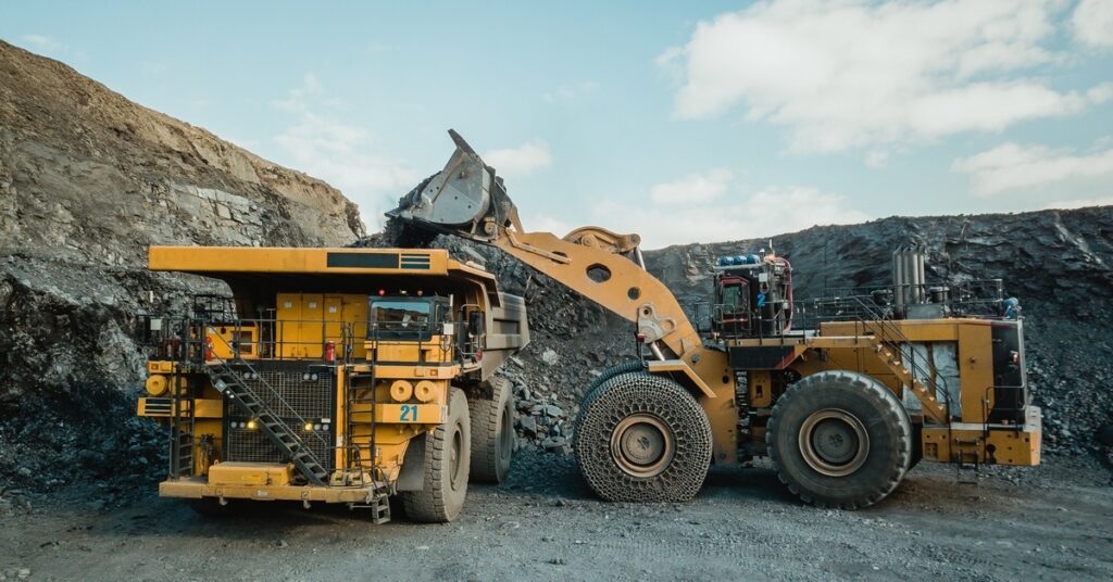 Two mining vehicles work together in the middle of a mining quarry. A wheel loader loads ore into a dump truck.