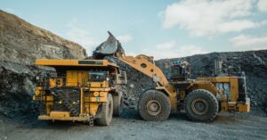 Two mining vehicles work together in the middle of a mining quarry. A wheel loader loads ore into a dump truck.