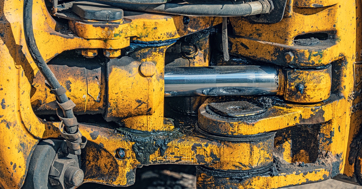 A close-up of the hydraulic system on a yellow mining machine that is covered in dried black residue.