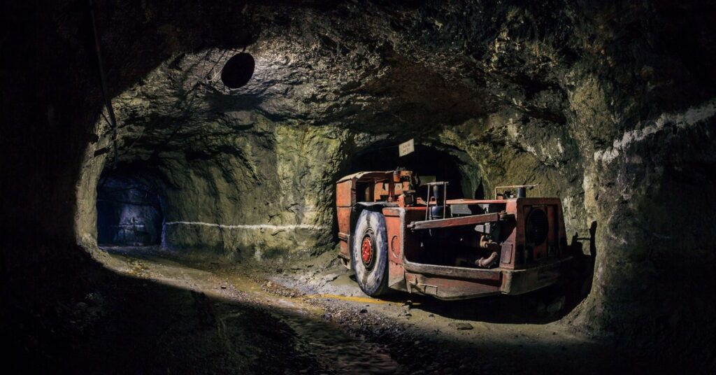 An unattended mining machine sits in a nook of a mining tunnel and lights up the path in front of it.