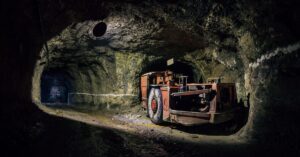 An unattended mining machine sits in a nook of a mining tunnel and lights up the path in front of it.