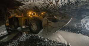 A large yellow load haul dumper machine drives through an underground mine with lights on top of it.
