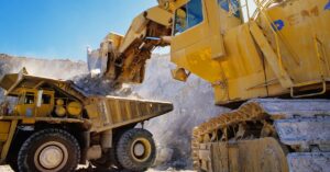 A large piece of mining equipment moves material into the back of a yellow truck at a mining site.