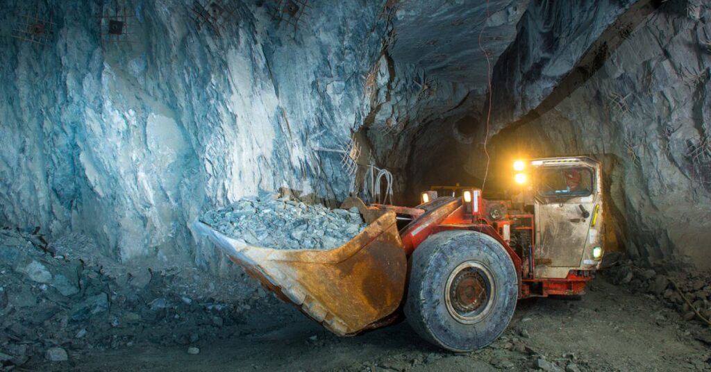 A mining vehicle parked inside of a cave system. The bucket of the vehicle is filled with rock and gravel.
