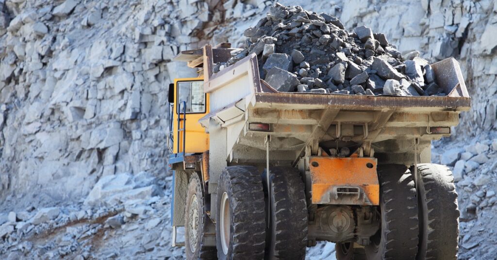 A bulldozer hauling large rocks in the vehicle’s bucket. The bulldozer is driving through a large mining site.