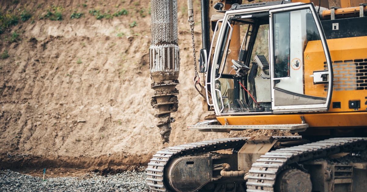 A mining vehicle with a large drill at a mining site. The vehicle has a clear sliding door and tracked treads.