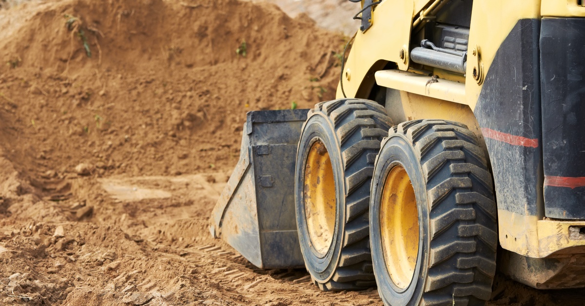 A bulldozer parked on top of orange sand at a mining site. The bucket on the bulldozer is set close to the ground.