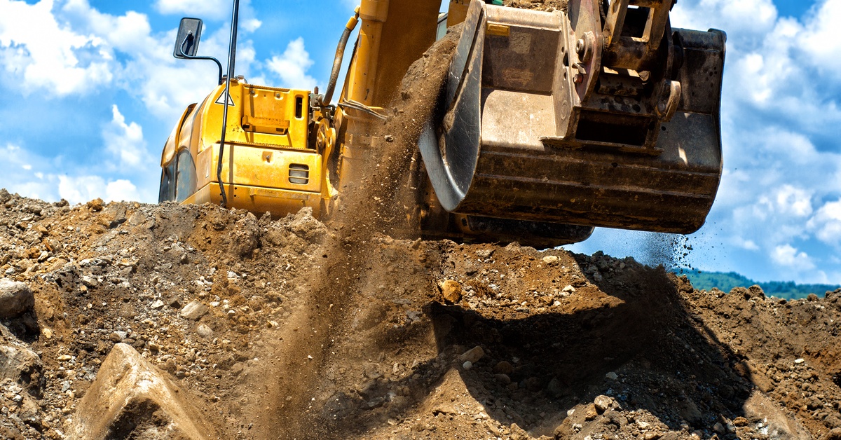 A mining excavator shoveling dirt and gravel from the bottom of a trench. There is dirt pouring out from the side.