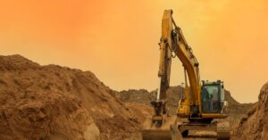A mining excavator parked in the middle of a sand and gravel quarry. The sky is shades of orange and yellow.