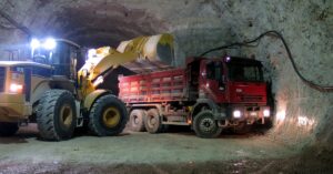 A bulldozer and a cargo truck parked in an underground mine. The headlights on the vehicles illuminate the tunnel.