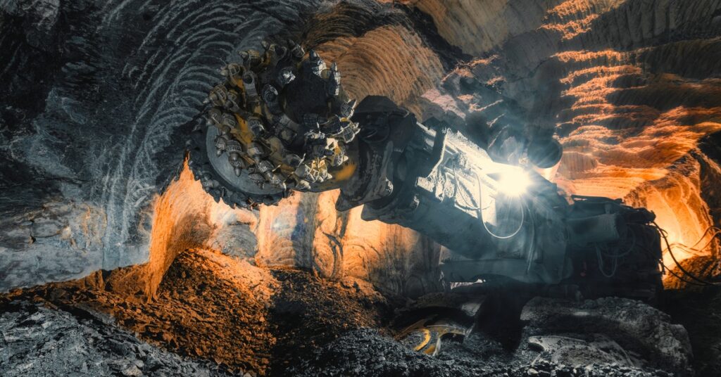 An off-highway vehicle inside an illuminated underground mine. There is a large drill attachment at the front of the vehicle.