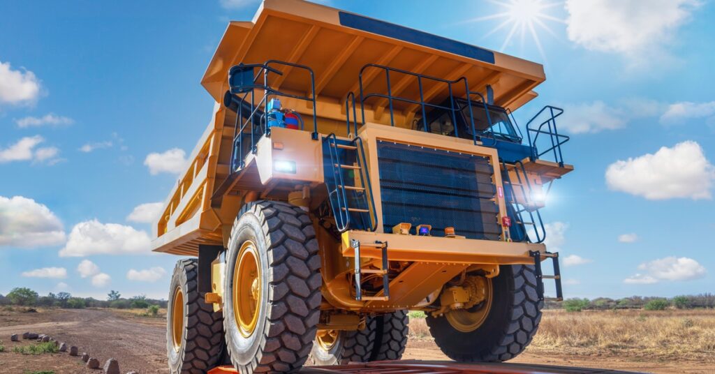 A large mining vehicle driving onto a yellow ramp at an outdoor sight. The headlights on the vehicle are on.