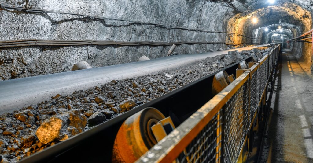 A conveyor belt system installed in an underground mine. The system transports black and gray ore down the tunnel.