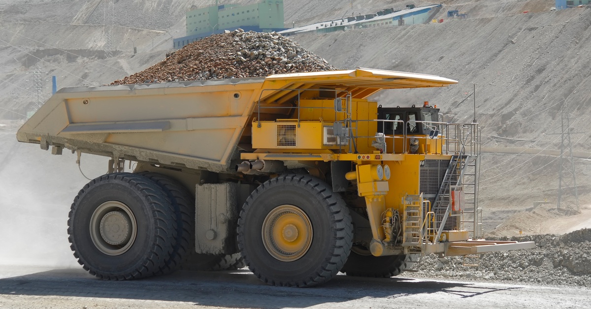 A heavy-duty mining vehicle transporting minerals and gravel in its bucket. The vehicle is parked at the bottom of a mine.