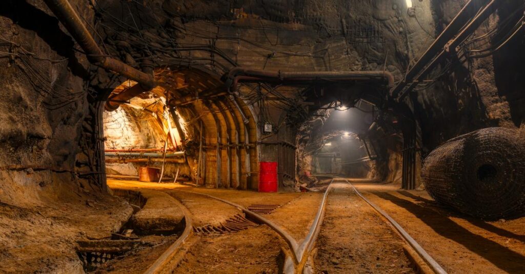 An underground mine with two illuminated paths. There are rail tracks leading down both sides of the mine.