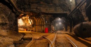 An underground mine with two illuminated paths. There are rail tracks leading down both sides of the mine.