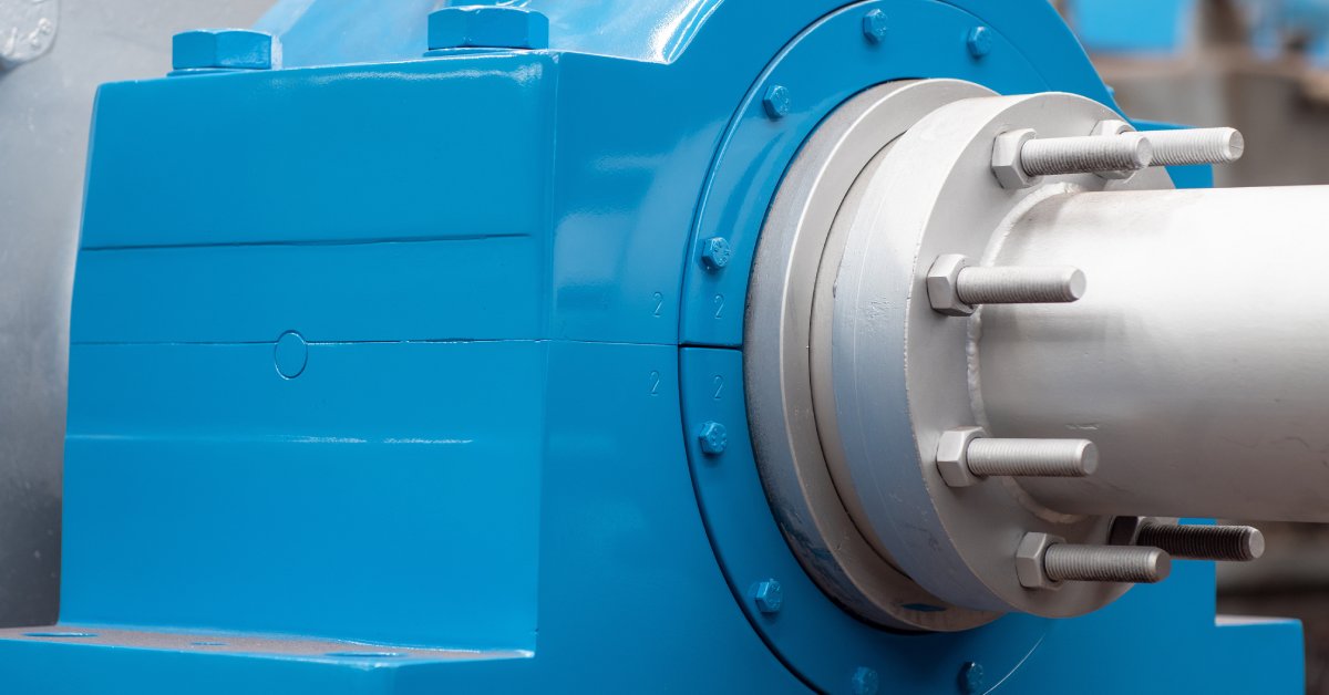 An extreme close-up of a blue bearing housing around a silver driveshaft. The equipment is inside a facility.