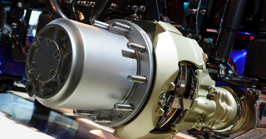 A close-up of an oversized wheel hub for heavy machinery. The equipment is elevated inside an enclosed facility.