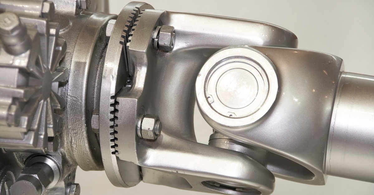 A metallic machinery component with bolts, a star-shaped gear, and a polished U-joint on a neutral background.
